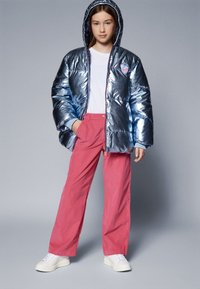 Blå metallisk boblejakke med hette, parret med rosa vide bukser og hvite sneakers. Hvit T-skjorte under.