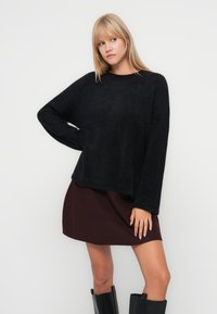 Pull noir en laine, fluffy, avec une coupe ample et un col arrondi, associé à une jupe bordeaux et des bottes noires jusqu'aux genoux. Texture lisse, design décontracté.