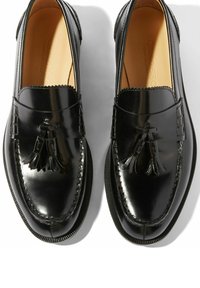 Crne kožne mokasine s sjajnim finishem, s ukrasnim resicama, okruglim vrhom i dekorativnim šavovima duž rubova.