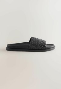 Sandales slides tissées noires présentant une semelle plate, une partie supérieure texturée et un design élégant avec un style glissant confortable.