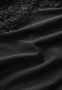 Tessuto di raso nero con una consistenza morbida; presenta un intricato pizzo nero lungo un bordo, creando un aspetto liscio ed elegante.