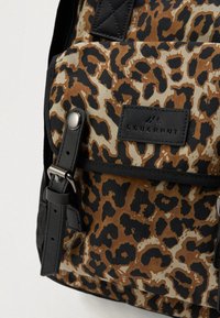Hnedo-čierny batoh s leopardím vzorom, čiernymi popruhmi a akcentmi, s obdĺžnikovou štítkou s logom a kovovou sponou.