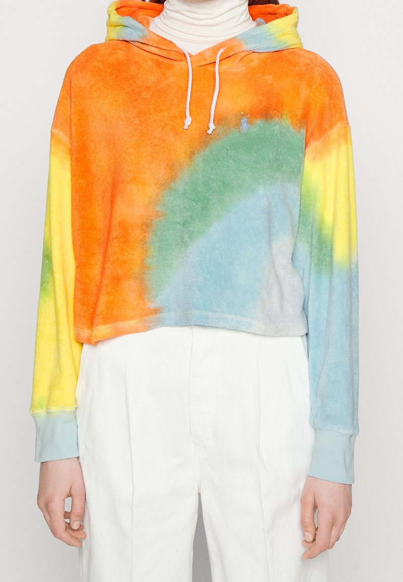 Felpa corta con cappuccio in fantasia tie-dye arancione, gialla, verde e blu. Tessuto morbido e vellutato con cappuccio regolabile tramite coulisse e polsini a coste.