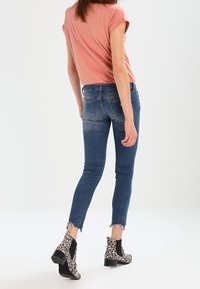 Jeans ajustados en denim azul medio con desvanecimiento, combinados con una camiseta rosa de manga corta y botas de tobillo en estampado de leopardo en blanco y negro.