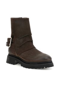 Bota de cuero marrón hasta el tobillo con punta redonda, diseño suelto, una hebilla decorativa y una suela robusta para mayor tracción.