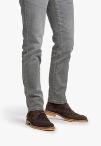 Gambe che indossano jeans slim-fit grigi e stivali alla caviglia in suede marrone scuro con suole in gomma marrone chiaro.