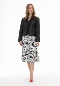 Sort læder cropped jakke med en enkelt knap, parret med en hvid nederdel med et sort abstrakt zebra-mønster, suppleret med røde højhælede sko.