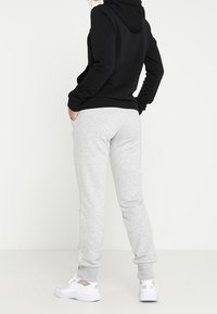 Sweat-shirt à capuche noir et pantalon de survêtement gris. Le tissu semble doux ; le pantalon a des poignets élastiques. Chaussures de sport blanches avec un détail logo.