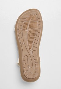 Sandalo di colore chiaro con suola in gomma testurizzata. La suola presenta un motivo ondulato per la presa, con scanalature che si estendono lungo la sua lunghezza.