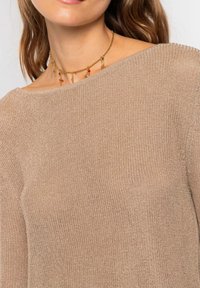 Suéter de punto beige con un amplio escote caído y tejido texturizado. Collar dorado con charms coloridos completa el look.