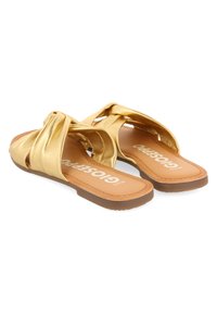 Sandalias deslizantes de metal dorado con correas anudadas, suela plana y plantilla marrón con el nombre de la marca grabado. Textura suave con un acabado brillante.