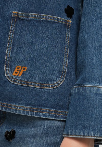Denim jakna z zadnjim žepom z oranžnim šivom in izvezenim logotipom "BP", ki je dopolnjena z detajlom v obliki črne cvetlice.