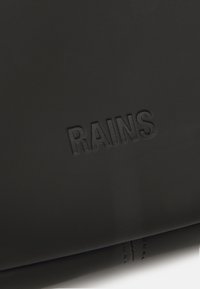 Juodas vandeniui atsparus medžiaga su iškilusiu "RAINS" logotipu. Lygus paviršius ir minimalistinis dizainas su matomais siūlų detalėmis palei kraštą.