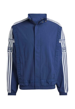 Tumši zilā jaka, izgatavota no viegla auduma, ar augstu apkakli, baltām svītrām uz piedurknēm un izteiksmīgiem Adidas logo abās pusēs.
