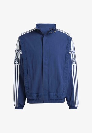 Temno modra jakna iz lahkega materiala, z visokim ovratnikom, belimi črtami na rokavih in izstopajočimi Adidas logotipi na obeh straneh.