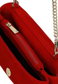 Červená semišová kabelka s jedním oddílem, která má kapsu na zip a řetízkový popruh ve zlaté barvě. Výrazné zapínání na druk na přední straně.