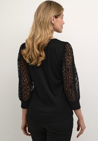 Black top with long lace sleeves featuring a floral pattern. The body is solid black with a round neckline and fitted design.