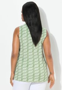 Top senza maniche verde con un motivo ondulato, caratterizzato da un design fluido e un tessuto morbido. Il retro presenta un orlo curvo e una texture liscia.