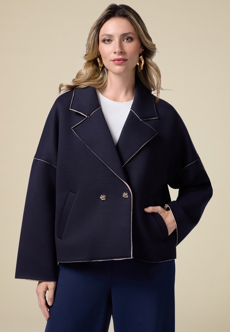 Giacca doppiopetto navy realizzata in tessuto strutturato, con ampi rever, due tasche frontali e cuciture a contrasto.