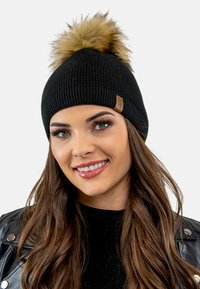 Zwarte gebreide beanie met een pluizige neppelzen pompon bovenop. Beschikt over een klein leren accentlabel en ribbeltextuur voor warmte.