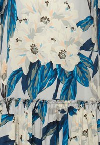 Kleid mit floralem Muster, das große weiße Blumen mit blauen und grünen Blättern zeigt, aus weichem Stoff und mit einem fransigen Saum.