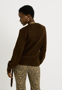 Suéter marrón de punto con mangas largas y un lazo en la cintura, combinado con pantalones de estampado de leopardo, que presentan una textura sutil.