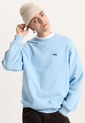 Lichtblauwe sweatshirt met een ronde hals, voorzien van een klein zwart "VANS"-logo op de borst. Gecombineerd met een beige gebreide beanie.