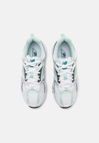 Białe sneakersy z miętowo-zielonymi akcentami, wykonane z siateczki i materiału syntetycznego, mają okrągły czubek i sznurowadła, z rozpoznawalnym logo marki na języku.