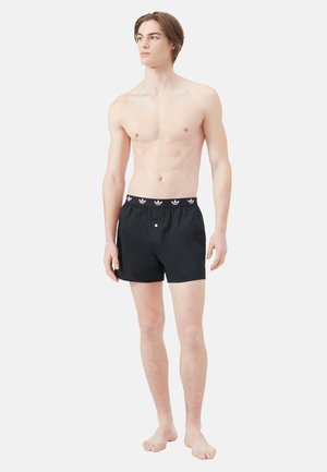 Schwarze Baumwollshorts mit einem elastischen Bund, der ein weißes Muster-Logo aufweist. Schlichtes Design mit einem Knopfdetail auf der Vorderseite.