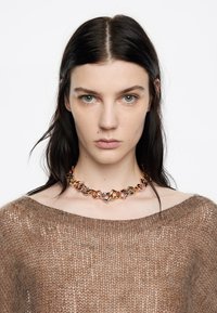 Collar de cadena metálica con eslabones geom�étricos entrelazados en tonos dorado, plateado y rosado, usado sobre un suéter marrón de punto suelto.