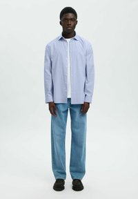 Lichtblauw overhemden met een ontspannen pasvorm, gecombineerd met losse, lichtgekleurde jeans en zwarte schoenen. Eenvoudig ontwerp, gladde textuur.