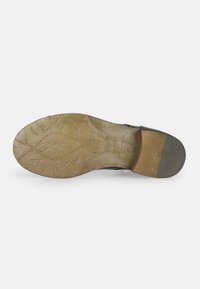 Sole di scarpa in pelle nera con motivi testurizzati, forma arrotondata, accento in marrone chiaro sul tallone e marchio visibile.