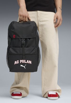 Schwarzer Rucksack aus strapazierfähigem Stoff mit Klappe, versehen mit rotem Logo und weißem Schriftzug "AC MILAN", Netzseitentaschen und einem Frontreißverschluss.