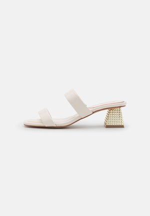 Åben tå beige sandal med to remme og en lav, firkantet hæl med guldnitter på hvid baggrund.