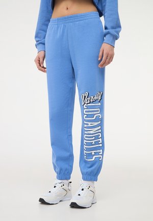 Pantaloni sportivi azzurri con vita elastica, polsini a costine e grande stampa bianca "Varsity Los Angeles" sulla gamba sinistra.