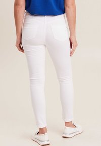 Witte skinny jeans met een hoge taille en twee achterzakken, gecombineerd met witte sneakers met een zilveren accent.