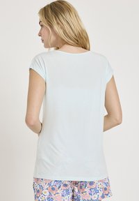 Ljusblå kortärmad t-shirt med rundad halsringning, slät textur och avslappnad passform, bärs tillsammans med färgglada blommönstrade shorts.