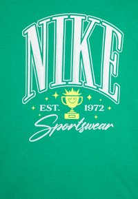 Groene katoenen t-shirt met opvallende witte "NIKE" tekst, een trofee graphic, "EST. 1972" en "Sportswear" in cursief. Zachte textuur.