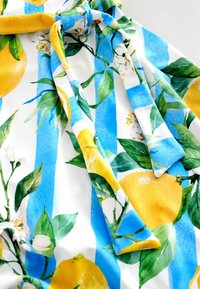 Stoff mit floralen Mustern, der gelbe Zitronen und grüne Blätter auf weißem Hintergrund mit blauen Streifen zeigt. Das Material wirkt glatt mit einer weichen Textur.