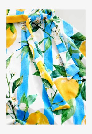 Blommönstrad tyg med gula citroner och gröna blad på vit botten med blå ränder. Materialet verkar slätt med en mjuk textur.