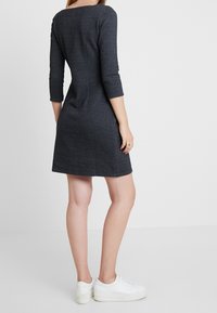 Laivastonsininen mekko, jossa on geometrinen kuvio, kolme neljännesosaa hihat, hieman kapeampi muotoilu ja pyöreä pääntie, yhdistettynä valkoisiin tennareihin.