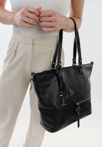 Schwarze Leder-Tote-Tasche mit strukturierter Oberfläche, doppelten Griffen, Reißverschlusstasche und einem dekorativen Quastenanhänger. Verfügt über Details in Silber.