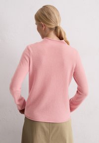 Jasnoróżowy, miękki sweter z okrągłym dekoltem i długimi rękawami, wykonany z teksturowanej tkaniny. Brzeg jest lekko zaokrąglony z tyłu.