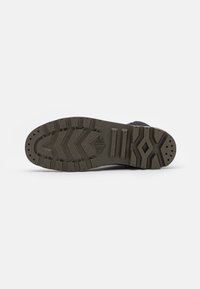 Suela de una bota Palladium gris que muestra profundas tracciones con patrones en forma de chevrón y geométricos sobre un fondo blanco.