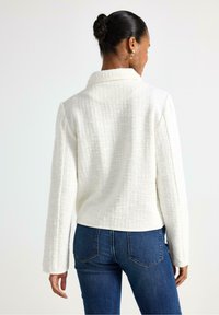 Giacca bianca strutturata con colletto a scialle, maniche lunghe e vestibilità cropped, abbinata a jeans scuri. Design semplice e pulito.