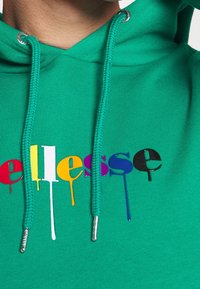 Felpa verde con cappuccio e lacci, caratterizzata da un logo colorato che gocciola in viola, blu, giallo, rosso e nero sul davanti. Decorazioni in metallo argentato.