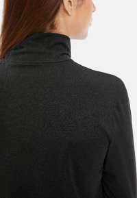 Schwarzer Rollkragenpullover aus glattem, strukturiertem Stoff. Mit hohem Kragen und subtiler shimmer, von hinten gesehen.