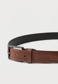 Svetlo rjav usnjen pas z notranjostjo v črni barvi, črnim kovinskim sponko in logotipom Valentino na traku blizu lukenj.