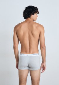 Boxer shorts gris avec une ceinture blanche affichant le texte "GANT". Le modèle est vu de dos, mettant en valeur une texture de tissu lisse.