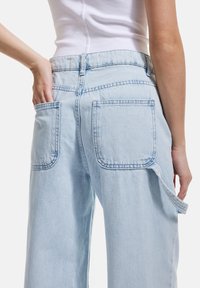 Ljusblå denimjeans med en avslappnad passform, med bakfickor, sömnadsdetaljer och en sidokrok för extra funktionalitet.